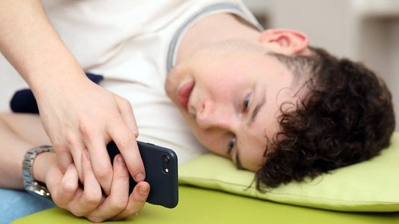 Teenager tippt im Bett auf seinem Smartphone herum. 