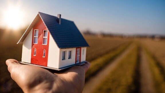 Symbolbild Hausbau - Hausmodell in einer Haus vor einer Ackerlandschaft