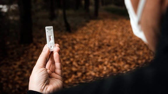 Ein Mann hält in einem Herbst Wald einen Covid-19 Coronavirus Schnelltest mit Testergebnis Positiv.