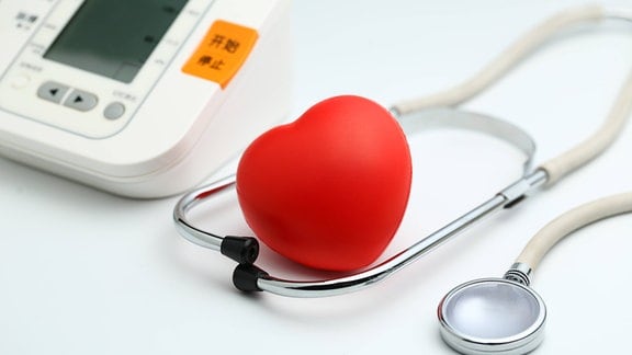 Elektronisches Blutdruckmessgerät, Stethoskop und rotes Herz auf weißem Hintergrund.