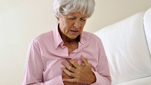 Seniorin hält sich vor Schmerzen die Hände an die Brust.