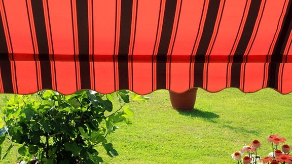 Markisen als Sonnenschutz. Eine Markise in leuchtender roter Farbe als Sonnenschutz über einer Terrasse im Sommer
