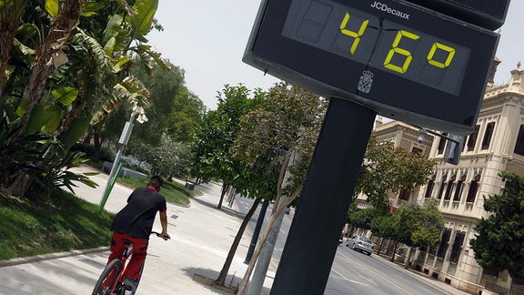 Ein Mann fährt am 12. Juli 2021 in der Stadt Murcia, Spanien, neben einem Thermometer, das 46 Grad anzeigt, Fahrrad. 