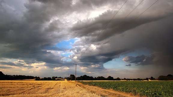 Dunkle Wolken über Feldern künden von einem nahenden Hitzegewitter.