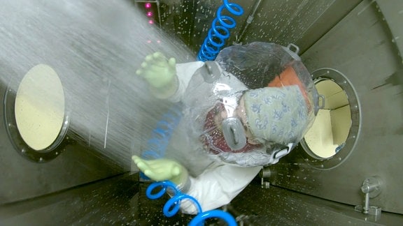 Ein Mann in einem Vollschutzanzug steht in einer Dusch-Schleuse unter einem Duschstrahl