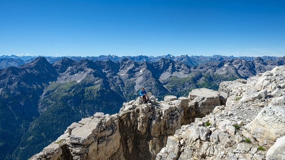 Wanderer sitzt auf Felsen, Aussicht vom Gipfel des Hochvogel