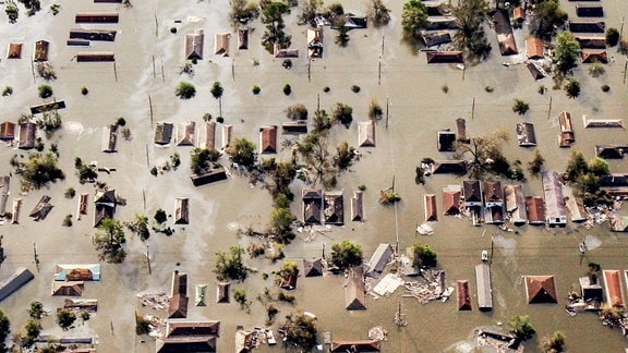 Ein dramatisches Bild. Ein Dorf nach einer Überschwemmung, aufgenommen aus der Vogelperspektive. Aus den trüben Wassermassen ragen nur noch die Dächer der Häuser und einzelne Telefonmasten heraus.