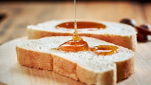 Honig wird auf Brotscheiben getropft.