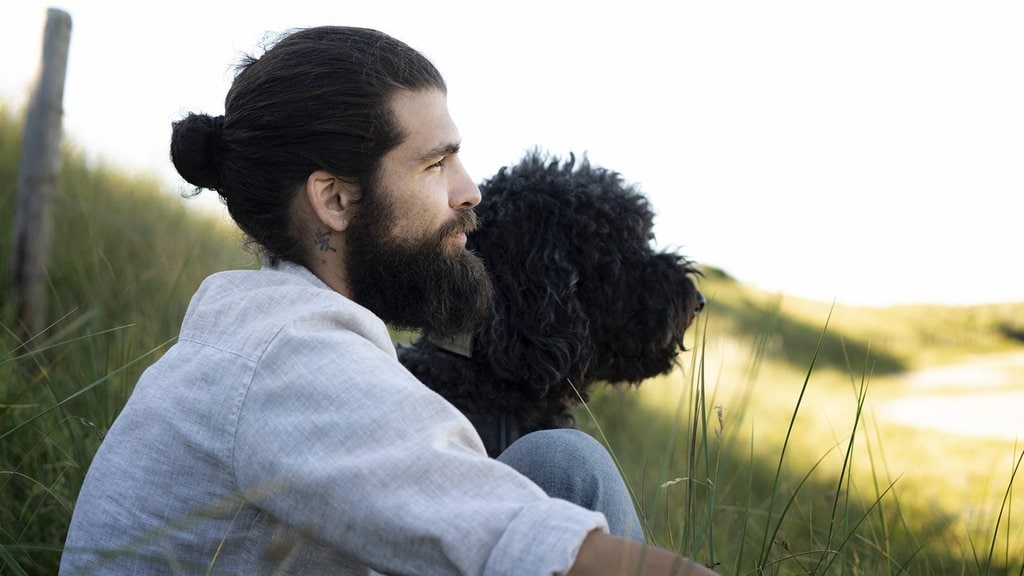 Junger Mann, der mit seinem Hund in den Dünen sitzt