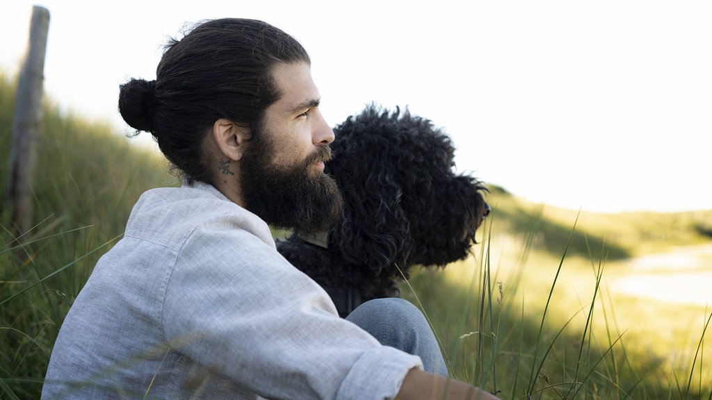 Young man sitting with his dog in the dunes