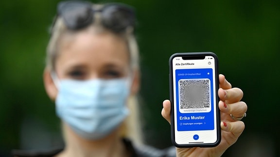 Symbolfoto Impfprivilegien, Frau zeigt App CovPass auf Smartphone mit digitalem europäischen Impfzertifikat inklusive QR-Code