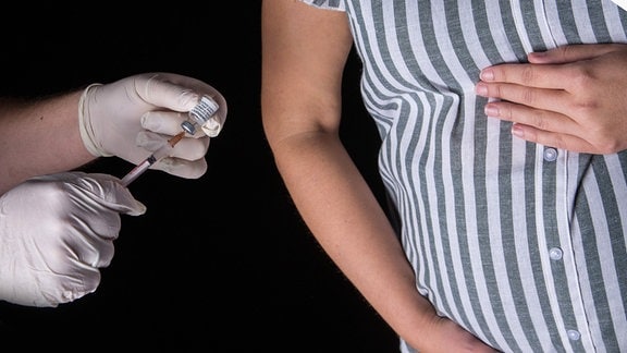 Eine Person mit Schutzhandschuhen hält eine Spritze neben einem Babybauch