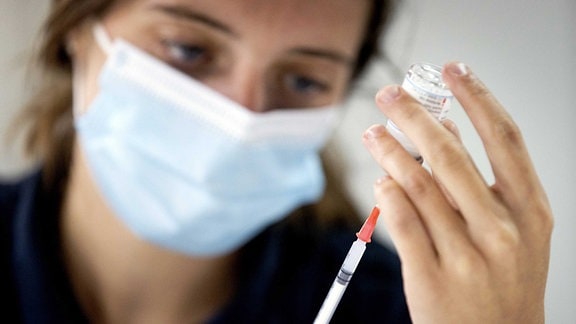 Eine Frau mit Mundschutz zieht eine Impfspritze auf.
