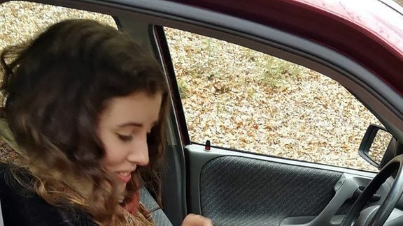 Junge Frau mit kleiner Eule auf dem Schoß auf einem PKW-Beifahrersitz
