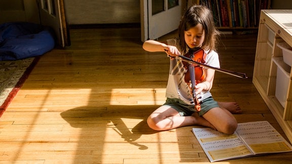 Mädchen sitzt auf dem Boden und spielt Geige.