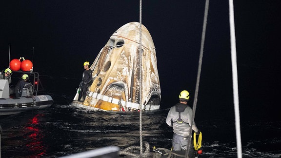 Ein Bergungsteams befördern das Raumschiff Dragon Endeavour von SpaceX auf das MEGAN Recovery-Schiff, kurz nachdem es im Atlantik verunglückt ist.