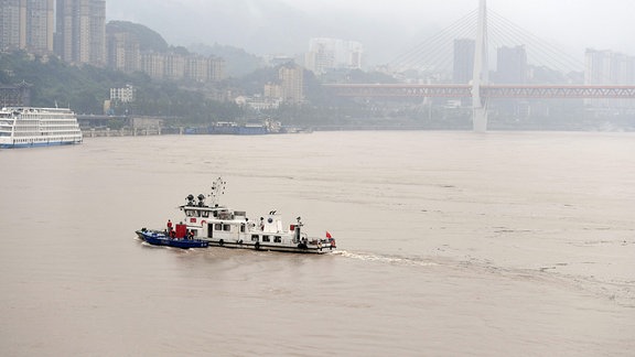 Schiff auf einem breiten Fluss (Jangtse) vor Stadtkulisse mit Brücke.