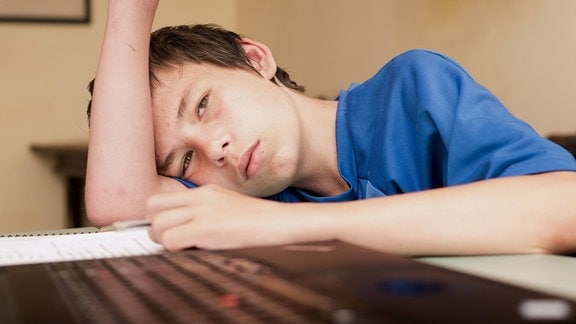 Teenager sitzt alleine lustlos bei den Hausaufgaben