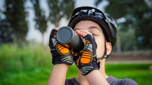 Junge mit Fahrradhelm trinkt aus Flasche