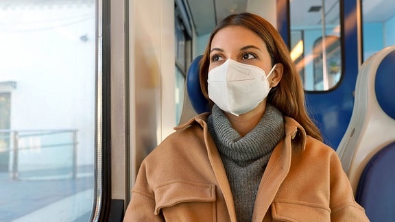 Eine junge Frau sitzt mit einer FFP2-Maske in einem Zug