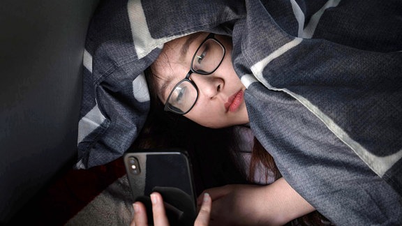 Ein Kind mit Brille liegt mit Handy im Bett