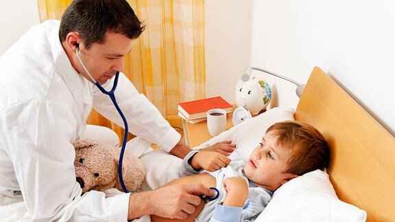 Ein Arzt untersucht bei Hausbesuch ein krankes Kind, das im Bett liegt