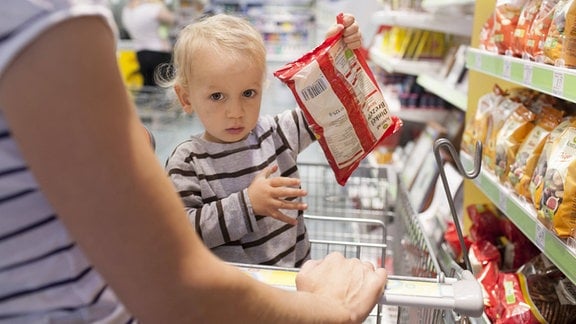 Kind im Einkaufswagen hält eine Tüte Brezeln.
