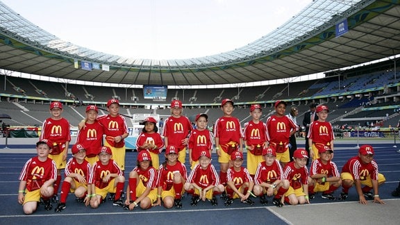 Kindergruppe wie Manschaftsfoto in Stadion mit Trikot auf denen das McDonald's M zu sehen ist