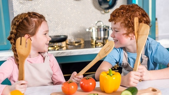 Zwei Kinder mit hölzernen Kochlöffeln in einer Küche