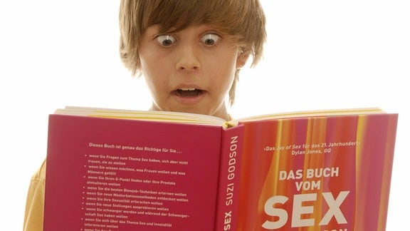 Sechzehnjähriger Junge mit Aufklärungsbuch, verwundert schauend