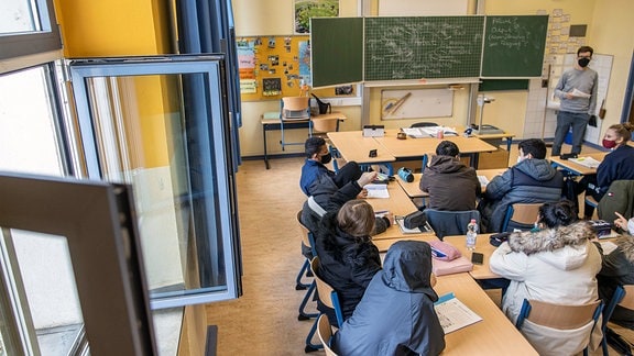 Schüler einer Gesamtschule sitzen in ihren dicken Winerjacken bei offenem Fenster in ihrem Klassenraum.