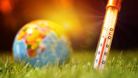 Fieberthermometer im Boden und Erdkugel, Symbolfoto Klimaerwärmung