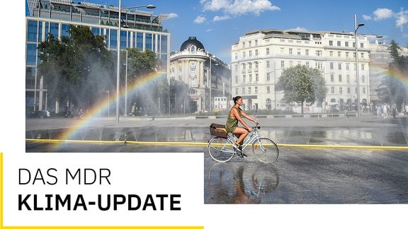 Das Bild zeigt eine Frau, die mit ihrem Fahhrand durch Wasserfontänen in der Wiener Innenstadt fährt. 