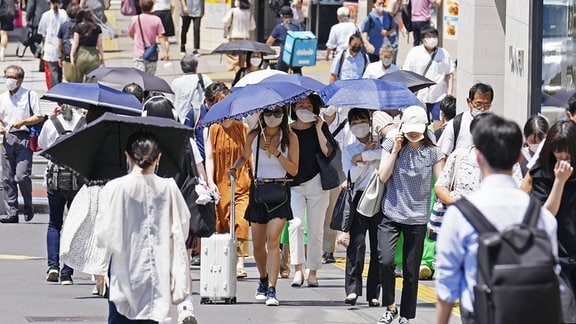 Menschen laufen mit Sonnenschirmen über die Straßen Tokios.