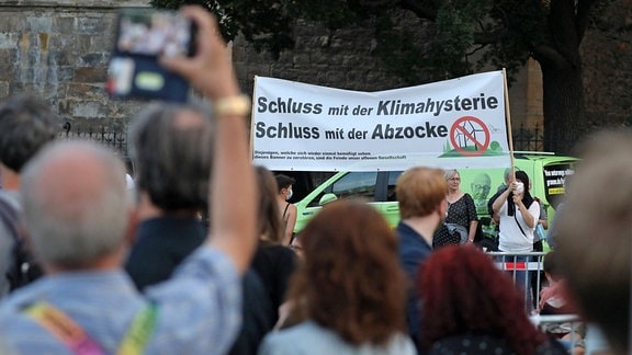Demonstranten einer Bürgerinitiative gegen Windräder halten ein Schild mit der Aufschrift - Schluss mit der Klimahysterie Schluss mit der Abzocke - nach oben