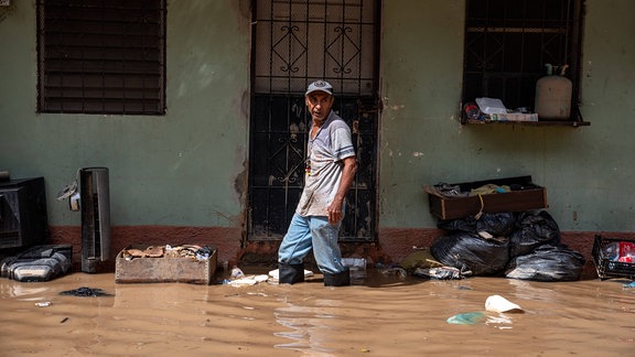 Ein Mann läuft durch kniehohes Wasser auf einer überfluteten Straße.