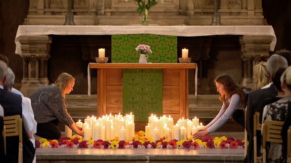 Viele Blumen und Kerzen werden vor einem Altar drapiert.