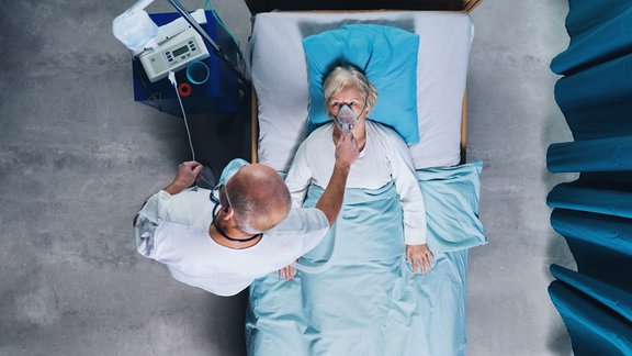 Arzt und infizierten Covid-19-Patienten mit Sauerstoffmaske im Bett im Krankenhaus