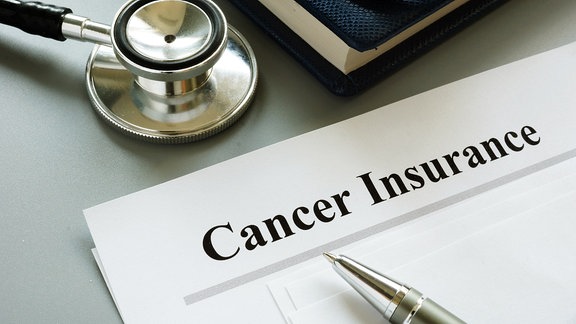 Auf einem Tisch liegt ein Stethoskop, ein Blatt mit der Überschrift 'Cancer Insurance' und ein Kugelschreiber.