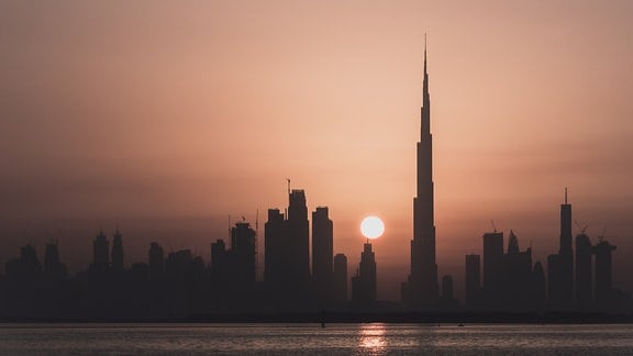 Stimmungsvolle dunkle Silhouette von Dubai bei Sonnenuntergang, Dunst und gelb-rosafarbenes Licht