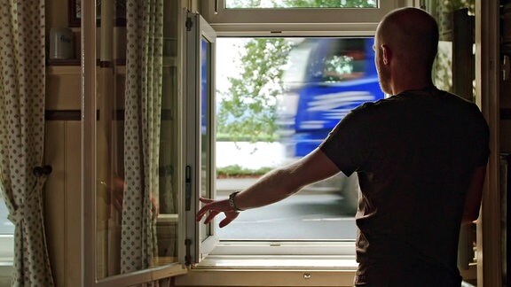 Ein Mann steht an einem geöffneten Fenster, an dem ein LKW vorbeifährt