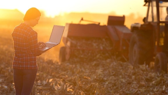 Junge Landwirtin mit Laptop auf dem Acker