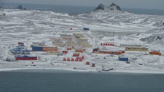 Siedlich mit containerartigen, roten Häuschen auf kargem, teilweise schneebedeckten Boden an einer Bucht