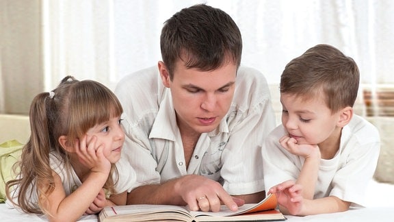 Vater liest mit zwei Kindern ein Buch.