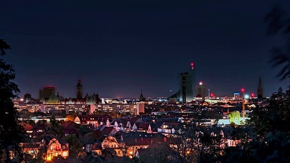 Skyline von Leipzig bei Nacht mit einigen Hochhäusern und Turmspitzen, die Hochpunkte wurden in einer Fotobearbeitung abgedunkelt um das Abschalten von Gebäudebeleuchtung zu symbolisieren.