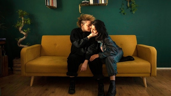 Zwei Frauen sitzen auf einem Sofa im skandinavischen Design und küssen sich zärtlich