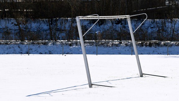 Einsames, etwas krumes Fußballtor ohne Netz im Schnee, im Hintergrund Gebüsch