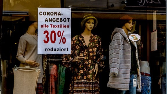 Hinweisschild in einem Schaufenster 'Corona-Angebot - alle Textilien 50% reduziert'