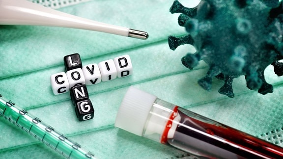 Buchstabenwürfel bilden den Schriftzug Long Covid neben Blutprobe und Coronavirus-Modell