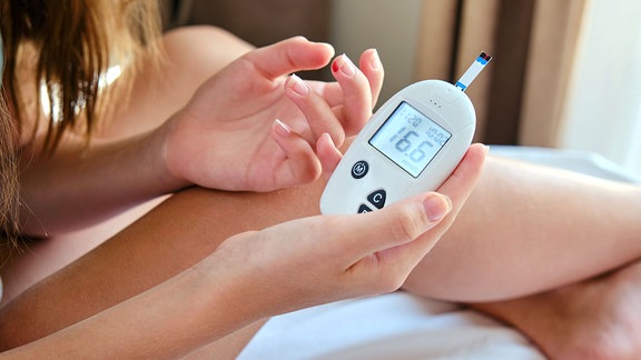 Ein junges Mädchen zeigt den Bildschirm eines Blutzuckermessgeräts mit den Ergebnissen eines Bluttests auf Diabetes in die Kamera.
